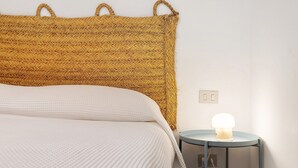 Een bed met een geweven hoofdbord, een nachtkastje met een lamp en een stopcontact aan de muur.