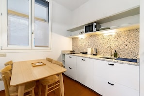 A compact kitchen with white cabinets, a granite countertop, a microwave, and a dining area with a table and chairs.