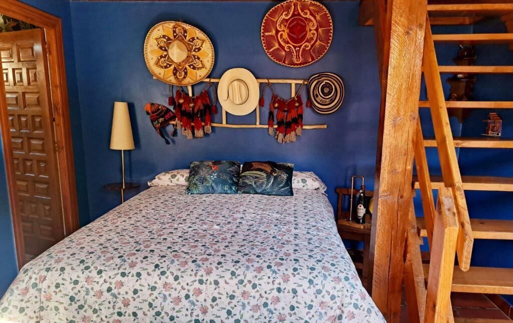 Un dormitorio con una cama, un estante de pared con objetos decorativos, una escalera de madera y una puerta.