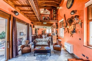 Amplia sala de estar con techo alto, vigas de madera y una chimenea acogedora. Hay sofás de cuero y una mesa de centro con libros.