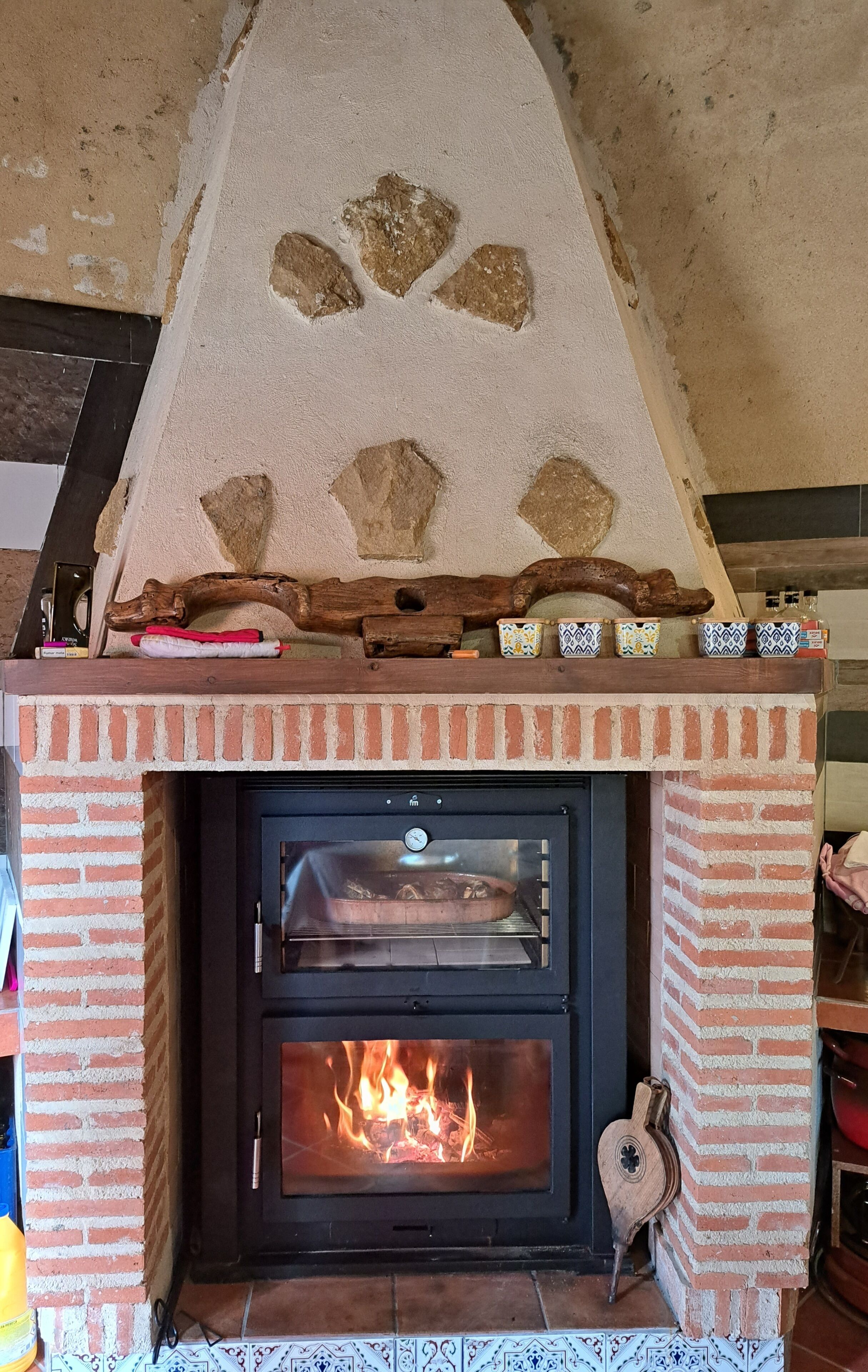 Ein Kamin aus Ziegelsteinen mit Glastür, in dem ein Feuer brennt, und ein dekoratives Stegmuster darüber.