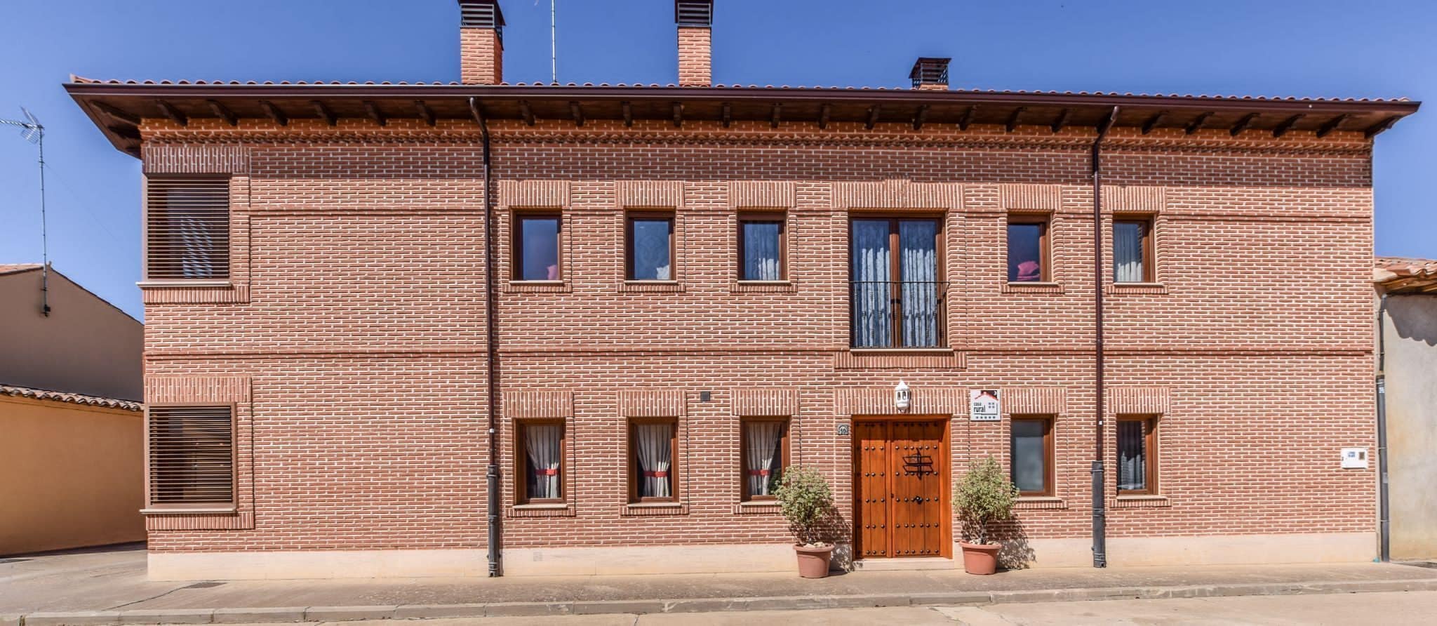 Edifici de maó de dos pisos amb una porta de fusta, diverses finestres i dues plantes en test a la façana.