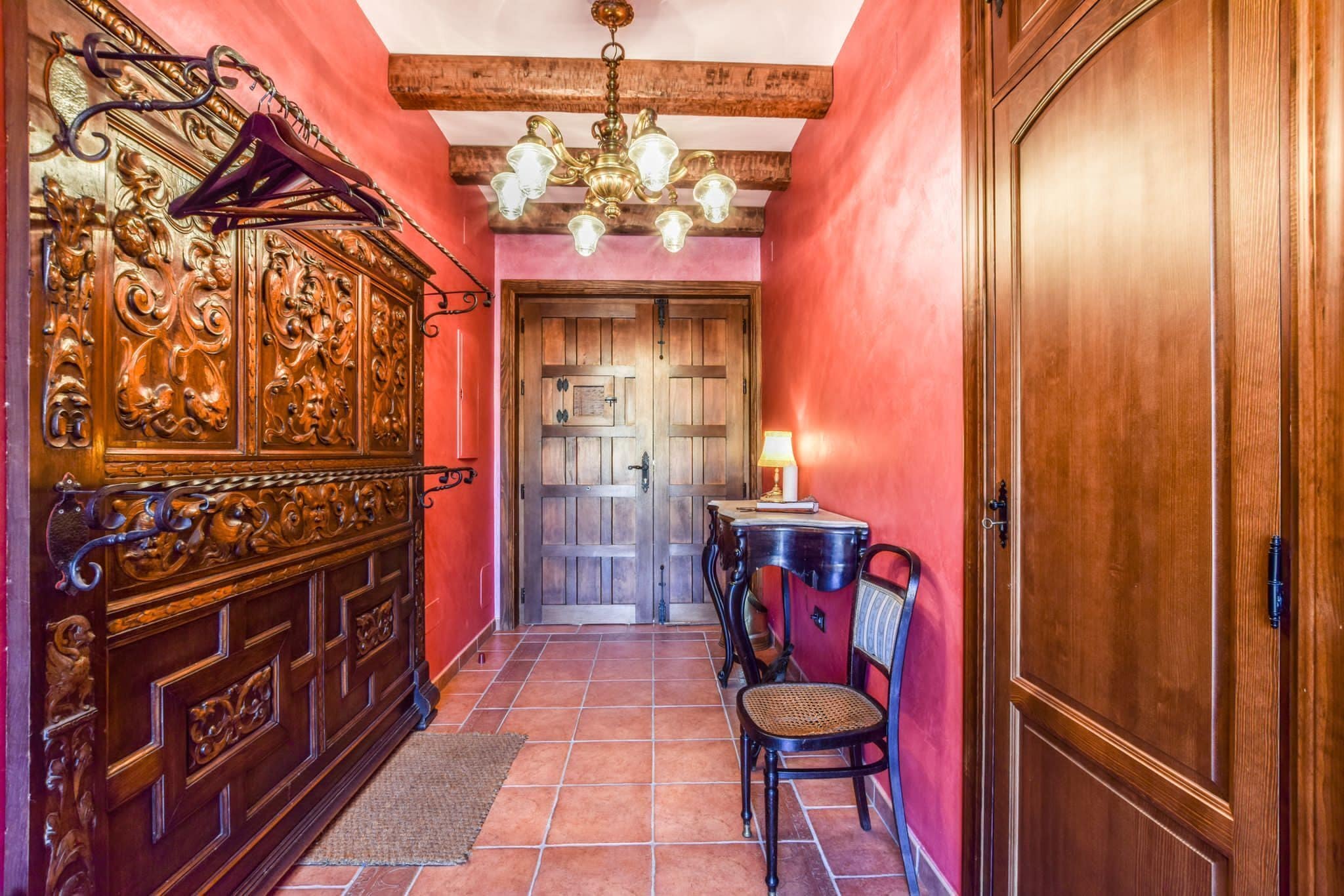 A hallway with a wooden cabinet, a chandelier, a table with a lamp, and a door.