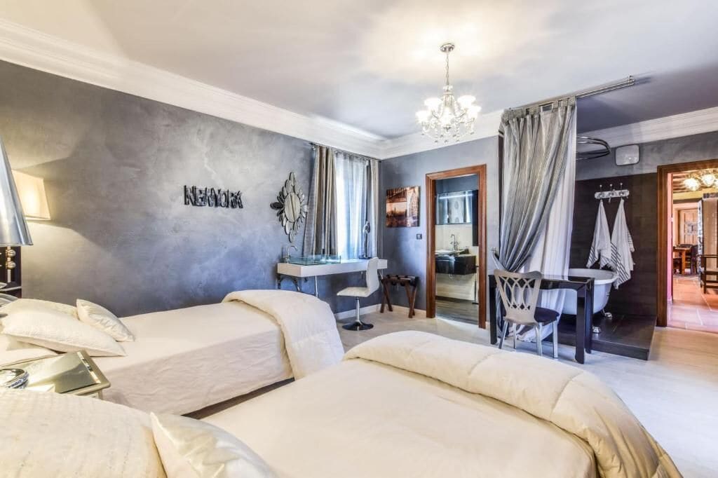 Ein Hotelzimmer mit zwei Betten, einem Schreibtisch, einem Stuhl, einem Schminktisch und einem Badezimmer mit Badewanne und Dusche.