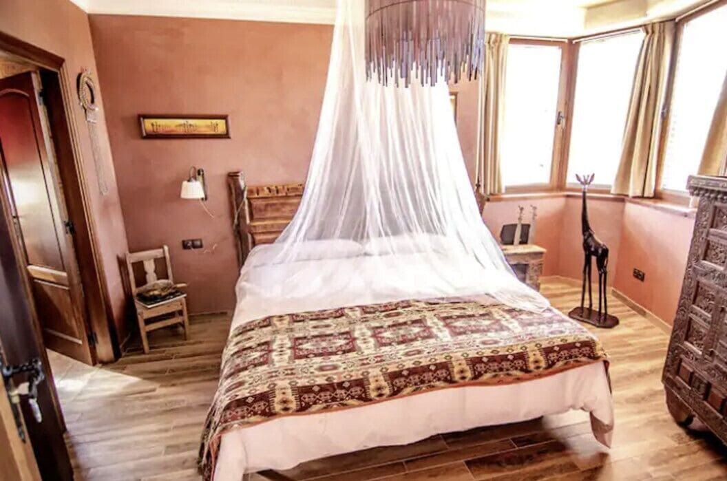 A bedroom with a four-poster bed, a canopy, a wooden dresser, and a chair.