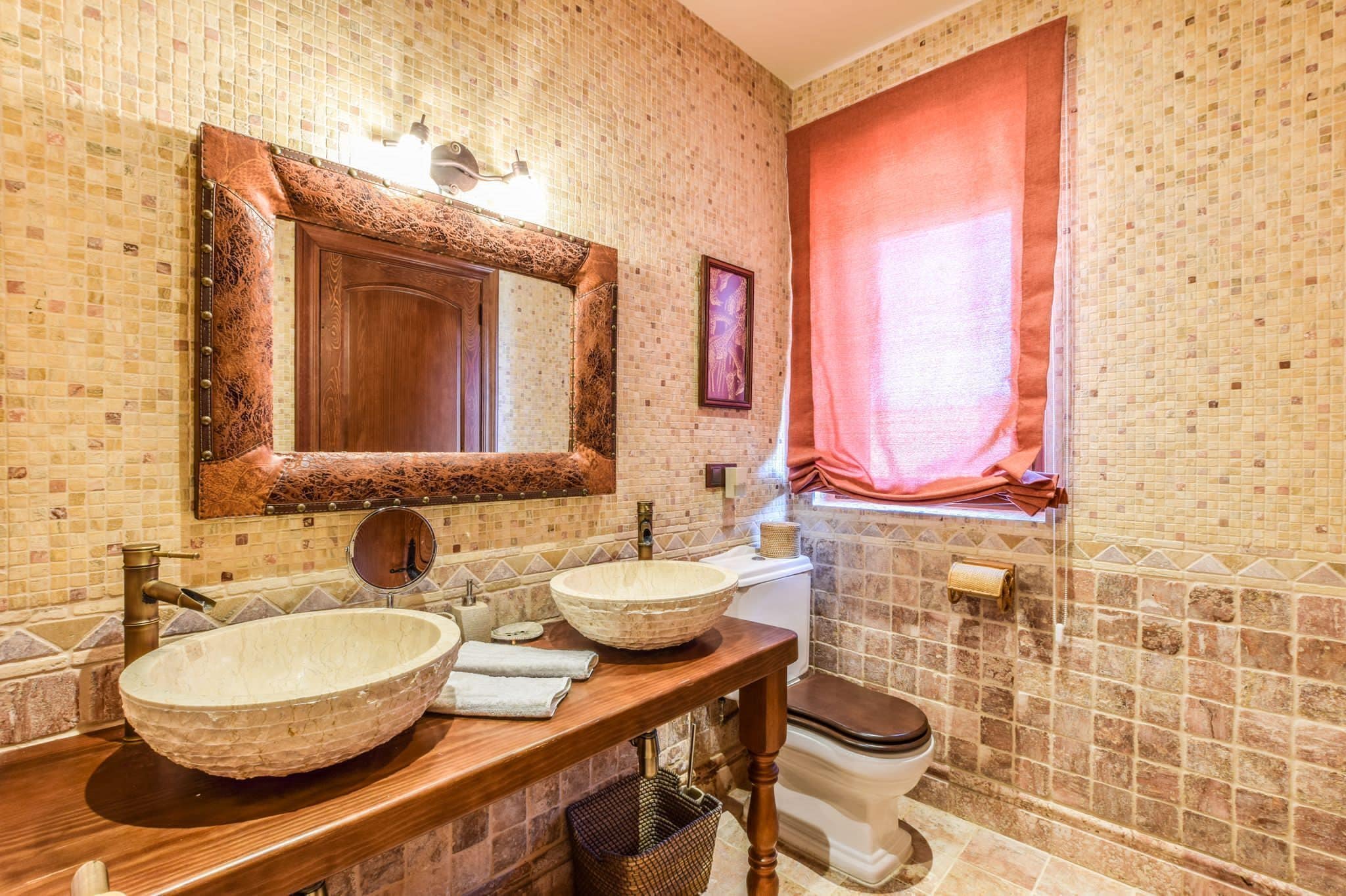 A bathroom with a wooden vanity, two sinks, a large mirror, and a toilet.