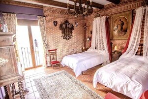 Una habitación con dos camas, una araña, un cuadro grande y una silla roja.