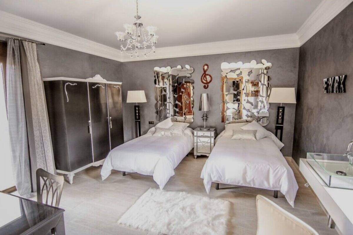 A bedroom with two beds, a chandelier, a wardrobe, and a mirror with decorative elements.