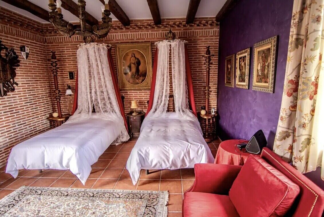 A room with two beds, a red sofa, a chandelier, and a painting on the wall.