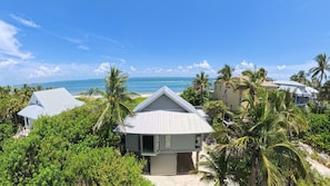 A beachfront property with multiple buildings, including a prominent house with a sloped roof, surrounded by lush greenery and palm trees. - Peters Beach House: Beachfront, Club Access & Dock (Captiva)