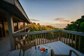 A wooden deck with a table and chairs, overlooking a beach and palm trees.
