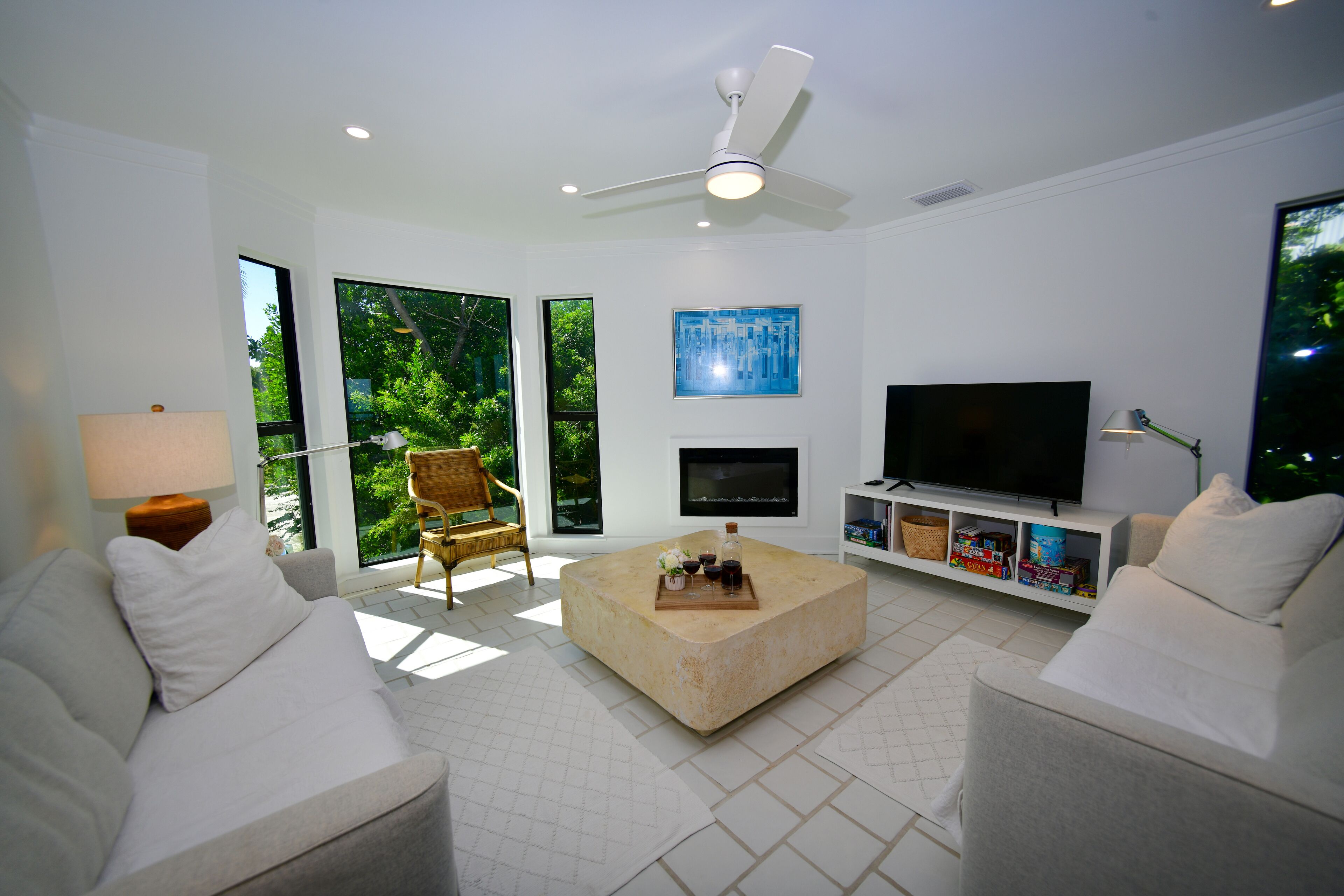 Ein modernes Wohnzimmer mit einer Couch, einem Couchtisch und einem Fernseher. Es gibt einen Deckenventilator, einen Kamin und ein Bücherregal.