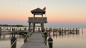A wooden pier leading to a gazebo with an American flag, extending into calm waters.