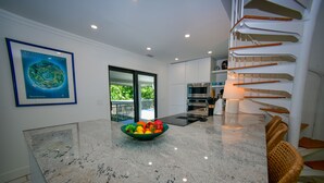 A modern kitchen with a granite countertop, a bowl of fruit, and a staircase with wooden steps.