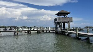 A pier with a wooden structure at the end, boats docked along the pier, and a clear sky with clouds.