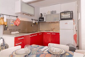Une cuisine de taille réduite avec des meubles de rangement rouges, un four à micro-ondes, un grille-pain et un réfrigérateur.