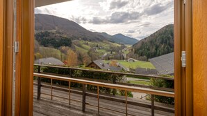 A wooden balcony with a view of a valley, houses, and mountains.