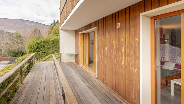 A wooden deck leading to a building with a glass door, a small table, and a view of a mountain.