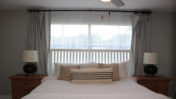 A bedroom with a large bed, two bedside tables with lamps, a window with curtains, and a ceiling fan. - 3-bedroom house in perfect location. 6 minutes from the Beach. (Vero Beach)