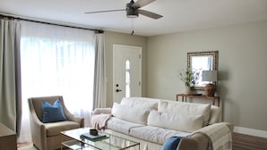 A living room with a beige sofa, a glass coffee table, a beige armchair, and a ceiling fan. - 3-bedroom house in perfect location. 6 minutes from the Beach. (Vero Beach)