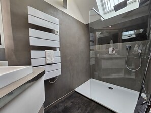 Ein modernes Badezimmer mit einer gläsernen Dusche, einem weißen Handtuch auf einer Ablage und einem Oberlicht.