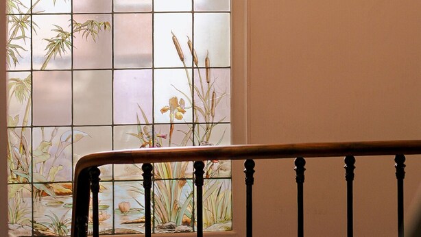 A staircase with a railing and a stained glass window with floral designs.