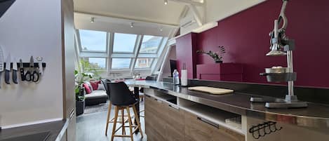 A modern kitchen with a wooden countertop, a dining area with a black chair, and a red accent wall.