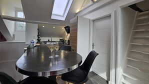 A modern kitchen with a skylight, a dining area with a round table and chairs, and a staircase leading to a second floor.