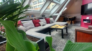 A modern living room with a high ceiling, skylight, a sofa set, a coffee table, and a TV mounted on a pink wall.