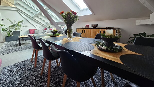 A modern loft-style dining area with a high ceiling and skylight, featuring a wooden dining table, black chairs, and a vase of flowers. - Loft-Executive-Garden view-Private Bathroom (Troyes)