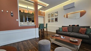 A modern living room with a grey sofa, ottomans, a wooden coffee table, and a kitchen area visible through an open door. - Loft-Executive-Garden view-Private Bathroom (Troyes)