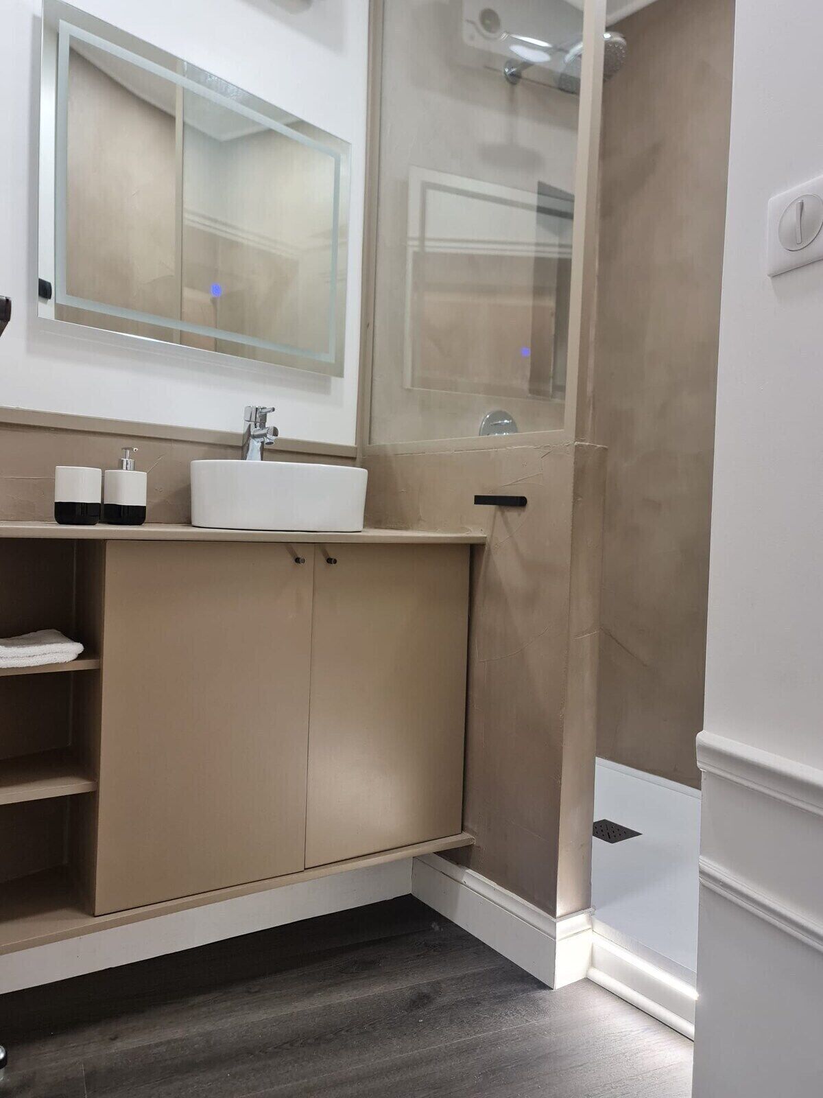 A modern bathroom with a beige vanity, a white sink, and a glass shower enclosure.