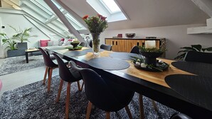 A modern loft-style dining area with a high ceiling and skylight, featuring a wooden dining table, black chairs, and a vase of flowers. - Apartment-Luxury-Private Bathroom-Garden view-Rdc A (Troyes)
