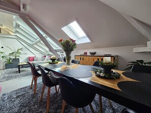 A modern loft-style dining area with a high ceiling and skylight, featuring a wooden dining table, black chairs, and a vase of flowers. - Apartment-Luxury-Private Bathroom-Garden view-Rdc A (Troyes)