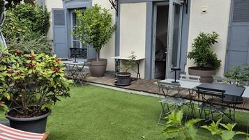 Une cour avec une pelouse artificielle, du mobilier d’extérieur, des plantes en pot et un balcon.
