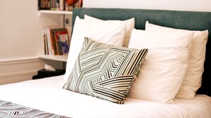 A neatly made bed with white bedding and a patterned pillow, a green upholstered headboard, and a bookshelf with books and decorative items in the background. - Apartment-Luxury-Private Bathroom-Garden view-Rdc A (Troyes)