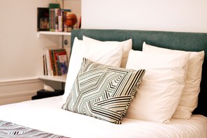 A neatly made bed with white bedding and a patterned pillow, a green upholstered headboard, and a bookshelf with books and decorative items in the background. - Apartment-Luxury-Private Bathroom-Garden view-Rdc A (Troyes)