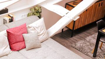 Un salon confortable avec un canapé, des coussins, un meuble en bois et une plante.