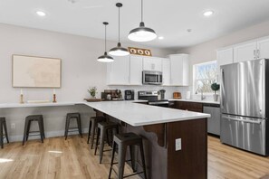 Una cocina moderna con una isla central, taburetes de bar, electrodomésticos de acero inoxidable e iluminación colgante.