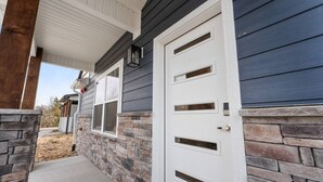 Une maison avec des fondations en pierre, une porte d’entrée blanche et un porche abrité.