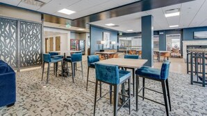 Moderni hotellin aula, jossa on baarialue, oleskelutiloja ja vastaanottotiski.
