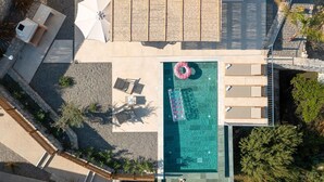 Vue aérienne d’un espace piscine sur le toit, avec une piscine rectangulaire, des chaises longues, un parasol et une terrasse en bois.