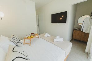 Une chambre d’hôtel avec deux lits, une table de chevet en bois sur laquelle se trouve un plateau de petit-déjeuner, un téléviseur fixé au mur, un miroir et une armoire en bois.