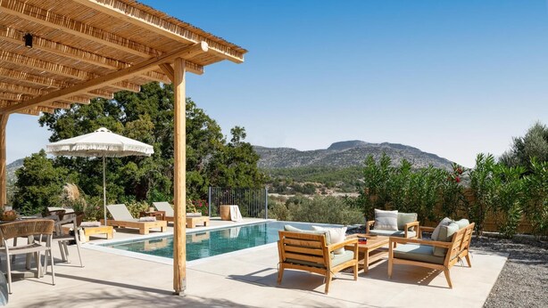 Area piscina con arredi in legno, una pergola e vista sulle montagne.