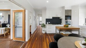 A modern kitchen with white cabinets, a wooden dining table, and a built-in oven. - Blue View Cottage! Simply Perfect! (Centenary Heights)