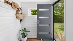 A modern entryway with a grey door, a small window, and a wall-mounted hat rack with a woven basket. - Blue View Cottage! Simply Perfect! (Centenary Heights)
