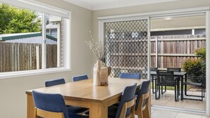 A dining area with a wooden table and blue chairs, a vase with branches, and a view of a backyard with a wooden fence and outdoor furniture. - Middle Ridge Retreat – Walk to Shops & Parks! (Middle Ridge)