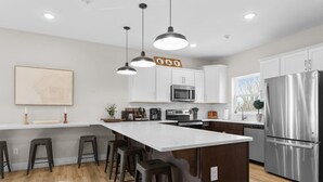 A modern kitchen with white cabinets, stainless steel appliances, a large island with bar stools, pendant lighting, and a view of the outdoors. - Gorgeous Lake View | Indoor Pool Access | Hot Tub (Branson)