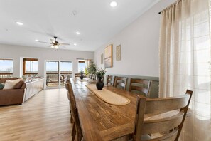 A spacious living area with a wooden dining table, a sofa, and a ceiling fan.