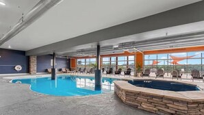 An indoor swimming pool with lounge chairs and a hot tub, large windows, and a stone wall. - Gorgeous Lake View | Indoor Pool Access | Hot Tub (Branson)